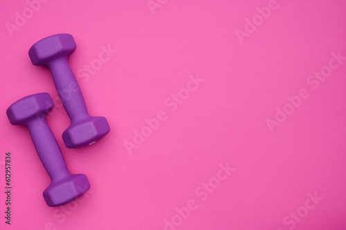 The layout of two rubberized dumbbells of 2 kg of purple color on a pink background, top view.Sports training