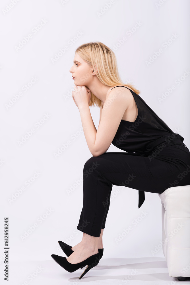 Fototapeta premium Portrait of a young and elegant girl sitting on a pouf on a white background.