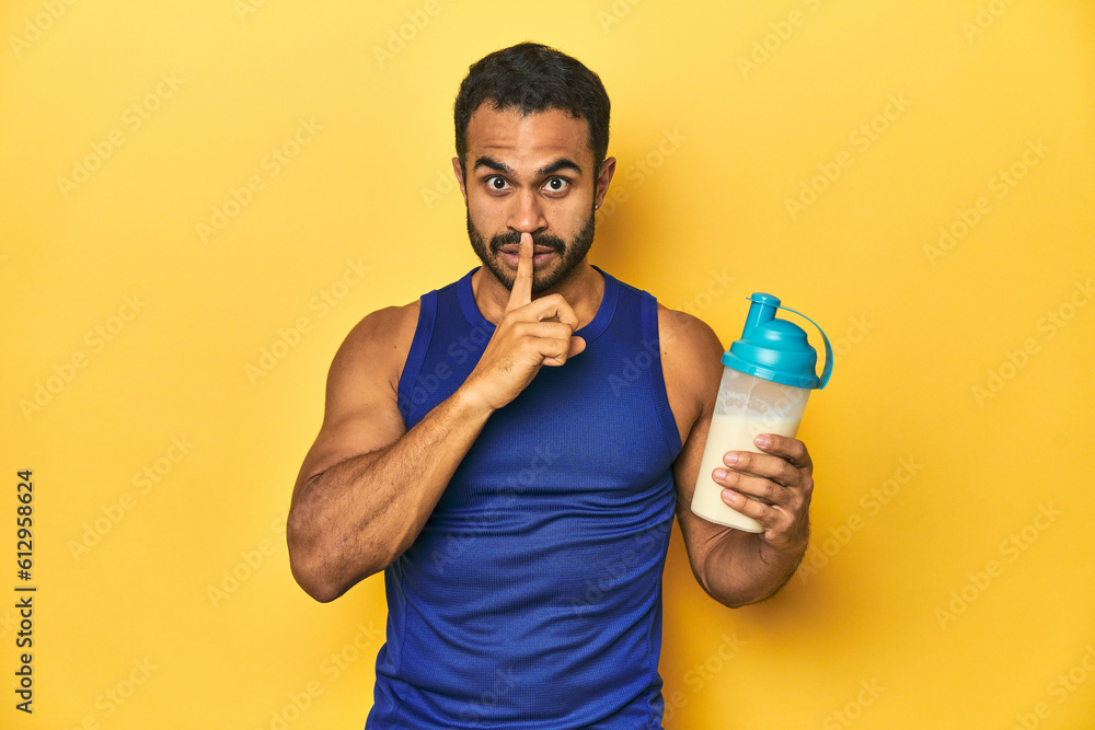 Athletic young Latino man holding a protein shake against a yellow background keeping a secret or asking for silence. Athletic young Latino man holding a protein shake against a yellow background keeping a secret or asking for silence.