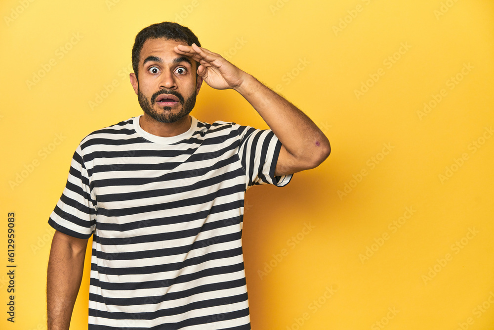 Casual young Latino man against a vibrant yellow studio background, shouts loud, keeps eyes opened and hands tense. Casual young Latino man against a vibrant yellow studio background, shouts loud, keeps eyes opened and hands tense.
