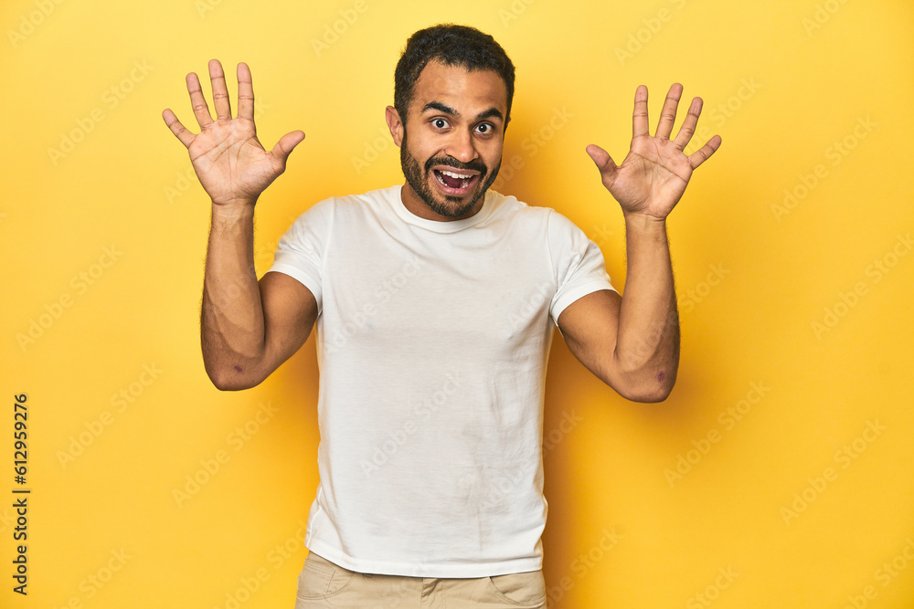 Casual young Latino man against a vibrant yellow studio background, receiving a pleasant surprise, excited and raising hands. Casual young Latino man against a vibrant yellow studio background, receiving a pleasant surprise, excited and raising hands.