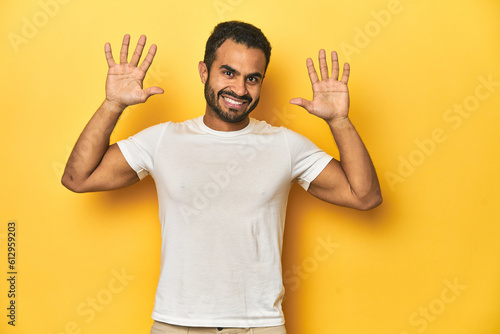 Casual young Latino man against a vibrant yellow studio background, showing number ten with hands. © Asier
