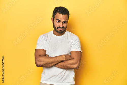 Casual young Latino man against a vibrant yellow studio background, unhappy looking in camera with sarcastic expression.