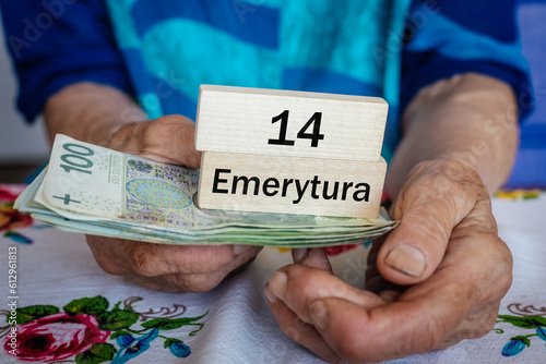 Polish pensioner holds money and wooden blocks with the inscription "14 pension" in Polish. Social concept. Additional 13th and 14th pensions for seniors in Poland
