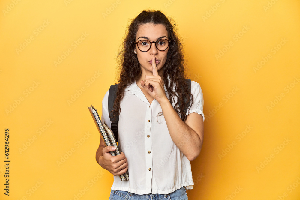 Student holding notebooks, glasses, backpack on, keeping a secret or asking for silence. Student holding notebooks, glasses, backpack on, keeping a secret or asking for silence.
