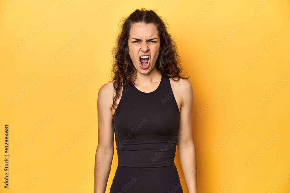 Sporty woman in active wear, yellow backdrop, screaming very angry and aggressive. Sporty woman in active wear, yellow backdrop, screaming very angry and aggressive.