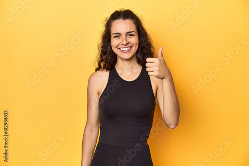 Sporty woman in active wear, yellow backdrop, smiling and raising thumb up
