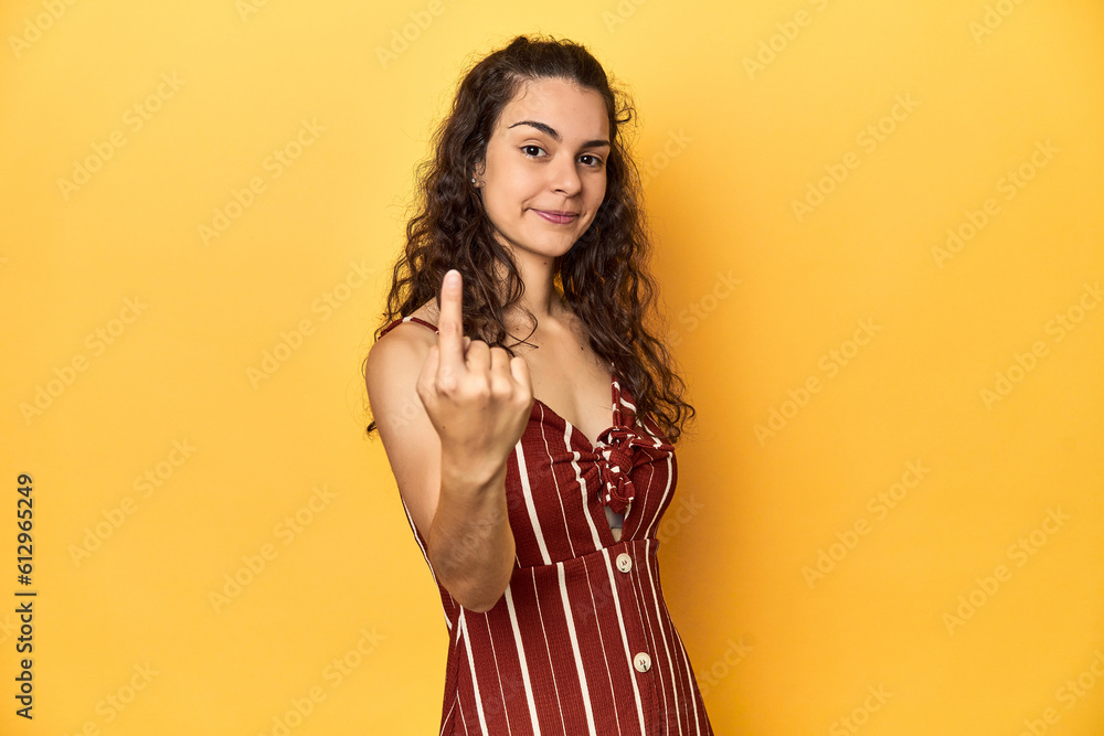 Young Caucasian woman, yellow studio background, pointing with finger at you as if inviting come closer. Young Caucasian woman, yellow studio background, pointing with finger at you as if inviting come closer.