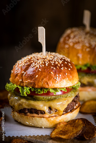 Tasty cheeseburger with lettuce, cheddar cheese, tomato and pickles. Burger bun with sesame seeds. Rustic atmosphere. Delicious fast food meal.