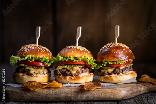 Fototapeta Naklejka Na Ścianę i Meble -  Three burger sliders placed on a wooden board in rustic atmosphere. Very tasty burgers with melted cheese, lettuce, tomato and sauce