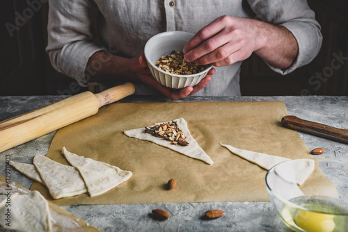 Croissant preparing. Baker sprinkles chopped almonds on top of hazelnut spread