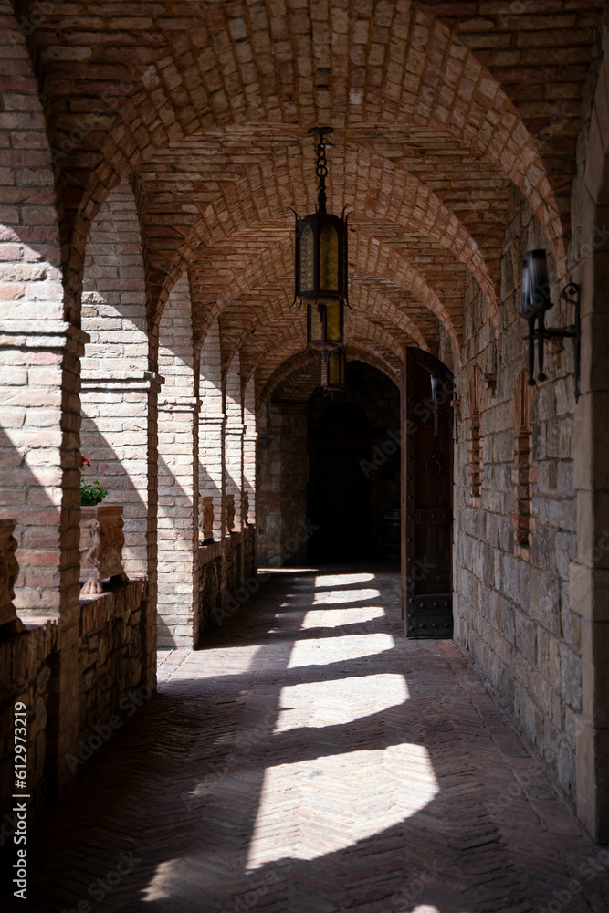 Sun light shinning through arched brick windows in a long castle corridor.