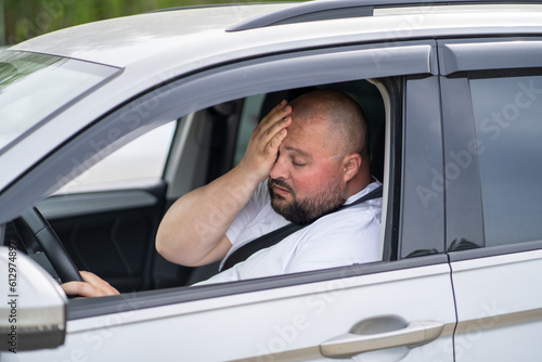 Tired overweight man drives car with broken air conditioner in hot summer weather. Male wiping sweat from face suffering from heat, stuffiness standing in road traffic. Exhausted overheated man.