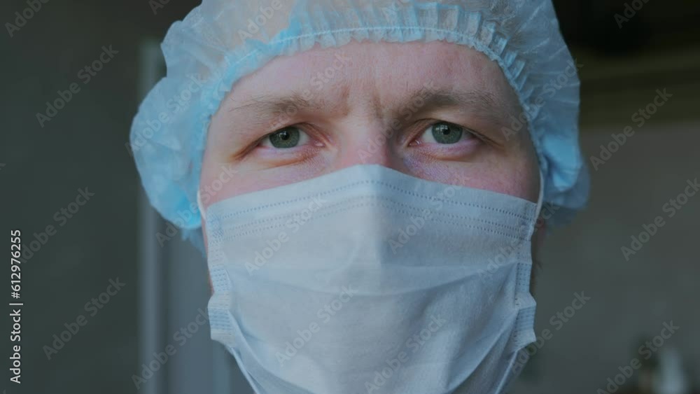 A young millennial male doctor looks into the camera with a calm, confident look. A man from the medical staff poses in front of the camera in a protective medical mask and a cap. High quality 4k A young millennial male doctor looks into the camera with a calm, confident look. A man from the medical staff poses in front of the camera in a protective medical mask and a cap. High quality 4k