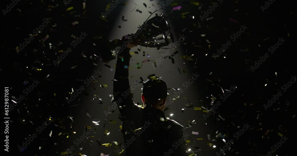 Silhouette of race car driver celebrating the win in a race against bright stadium lights, rising a trophy over his head