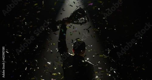 Silhouette of race car driver celebrating the win in a race against bright stadium lights, rising a trophy over his head