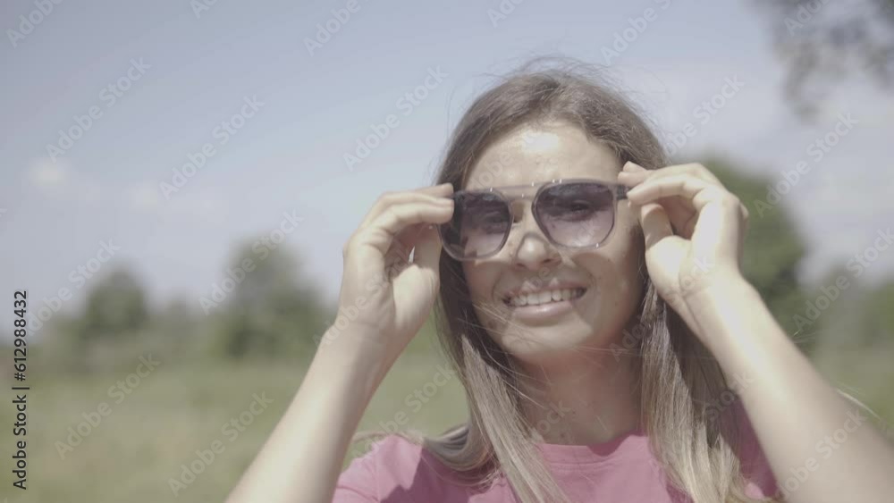the girl looks at the camera, smiles, puts on sunglasses and exposes her face to the sun. the girl looks at the camera, smiles, puts on sunglasses and exposes her face to the sun.