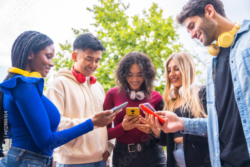 Low angle view of a group of young multi-ethnic teenage friends using cell phones on campus in the city. Technology addicted millennial community concept. Social Media communication generation Z