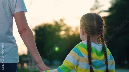 Little girl holds mom hand go in park. Mother daughter, holding hands, walking on summer sun day. Concept of family relations. Happy family mom child walking in outdoors. Child, parents walk, playing