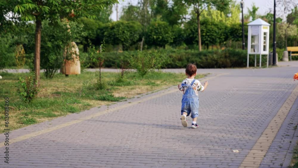 One year old toddler running in the beautiful summer park. Little kid runs by the paved road. One year old toddler running in the beautiful summer park. Little kid runs by the paved road.