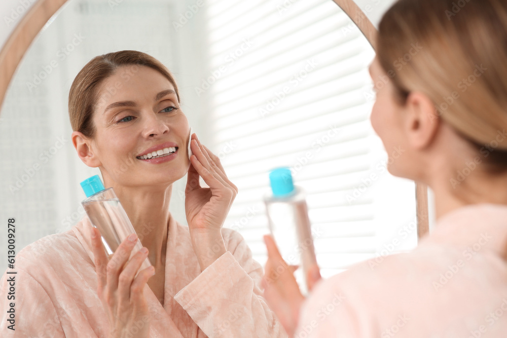 Beautiful woman removing makeup with cotton pad near mirror indoors Beautiful woman removing makeup with cotton pad near mirror indoors