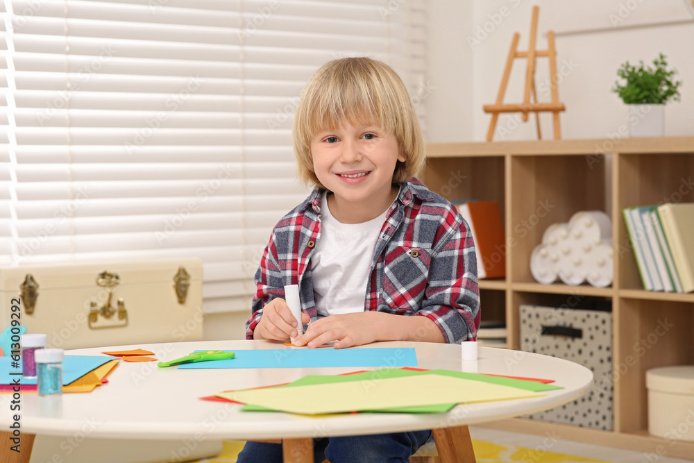 Cute little boy with glue stick at desk in room. Home workplace Cute little boy with glue stick at desk in room. Home workplace
