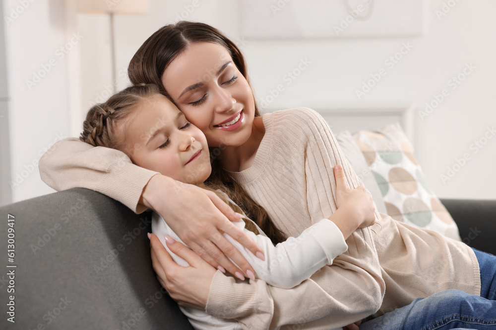 Happy mother hugging her cute daughter on sofa at home Happy mother hugging her cute daughter on sofa at home