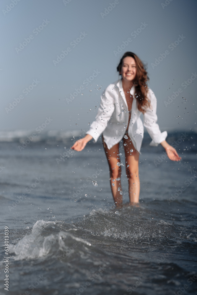 Young girl in bikini and white shirt playing with sea waves on the shore of a Balinese beach. Travel to tropical countries.