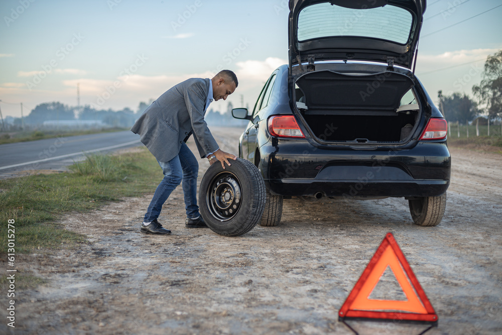 Latino man changes a flat tire on his car at the side of the road. Latino man changes a flat tire on his car at the side of the road.