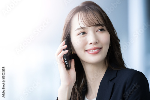 Close-up of a beautiful Japanese woman in a suit talking (contacting) on the phone. Copy space at left.