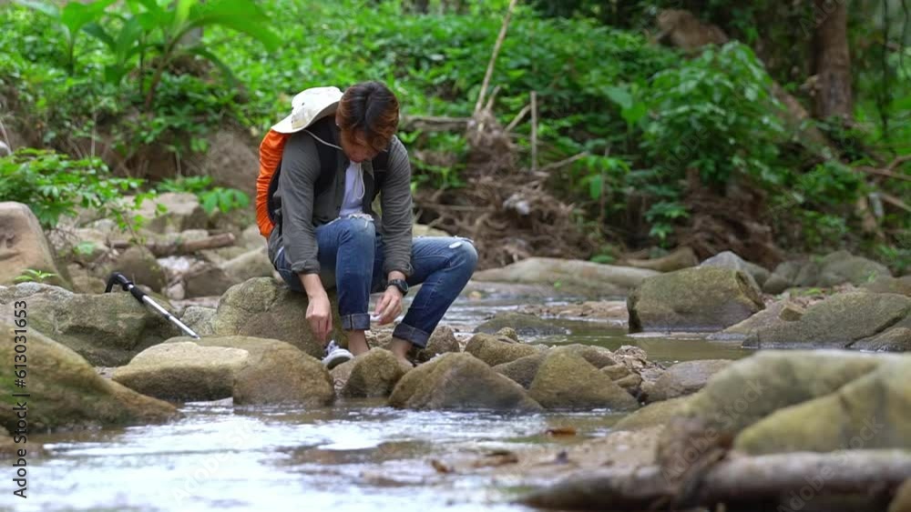 A young man who enjoys trekking for a leisure holiday rests. Stop to sit and rest by the stream to recover from exhaustion. Exciting adventure and trekking through beautiful nature. A young man who enjoys trekking for a leisure holiday rests. Stop to sit and rest by the stream to recover from exhaustion. Exciting adventure and trekking through beautiful nature.