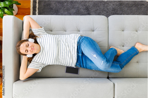 Woman in headphones laying, relaxing on a comfortable couch, listening to music