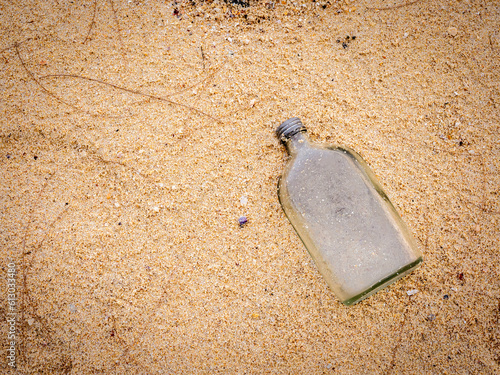 Glass flat bottle on sandy beach with copy space, top view. Close-up empty uncapped used liquor bottle piled up with sand, dumped on the beach. Polluted garbage abandoned by tourists. photo