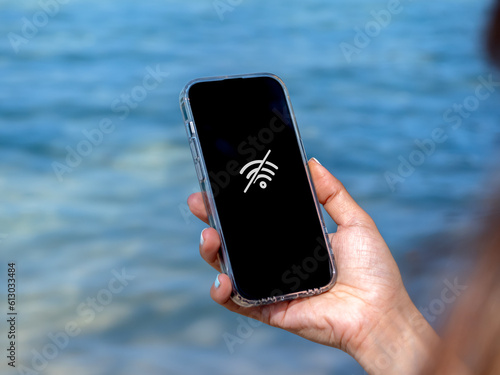 No internet connection technology concept. No signal service at the beach. Wi-Fi network offline sign on mobile smart phone display screen on woman\'s hand on blue tropical sea water background.