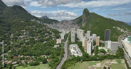 Flying backwards above road between mountains leading to Rio de Janeiro and tall buildings along San Conrado beach photo