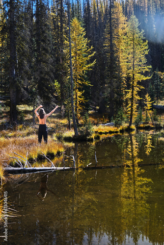 Woman by serene lake with reflections of yellow trees enjoying the nature. Colorado. United States of America