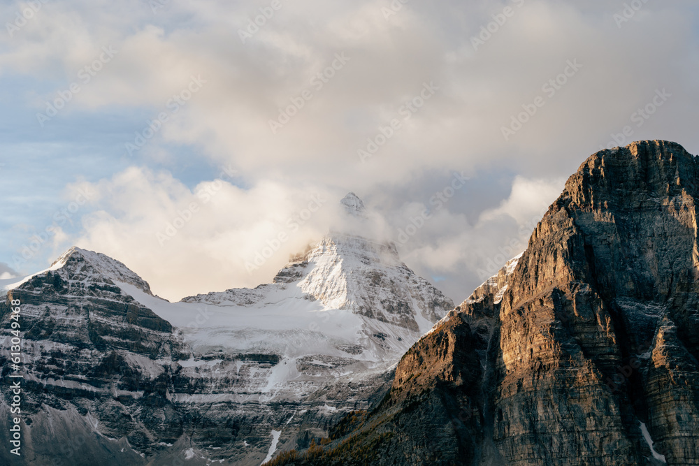 grande montagne avec sommet enneigé sous les nuages lors d'un lever de soleil en automne et montagne rocheuse devant