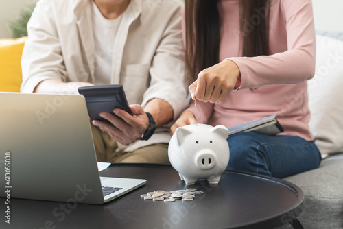 Happy asian young couple love hand calculate, putting coin in piggy bank for saving money to buy real estate for new home. Business finance, deposit with banking for financial planning future together