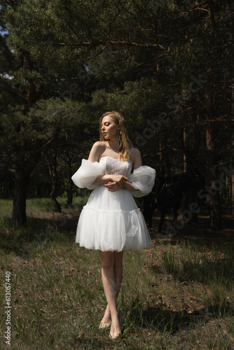 A beautiful caucasian girl in a wedding dress stands in the forest under the sunlight