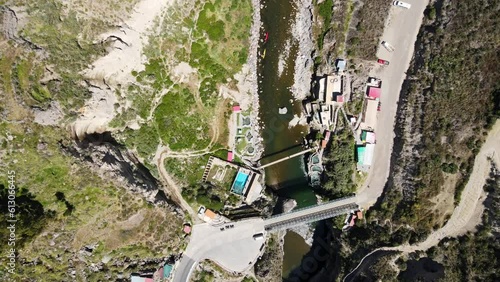Aerial shot drone descends with camera facing down over Calera thermal baths and people walking across pedestrian bridge crossing river photo