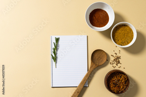 Directly above shot of spices in bowls with notepad and rosemary on beige background, copy space