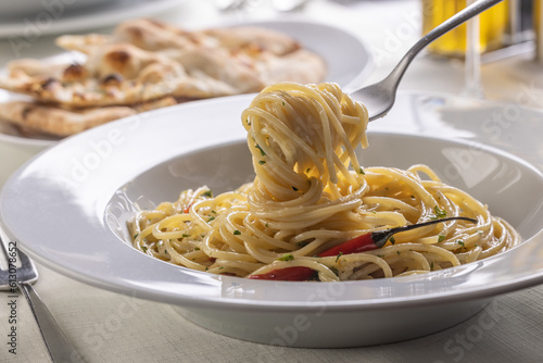 Spaghetti aglio e olio spinned on a fork taking a mouthful portion of pasta out of the plate