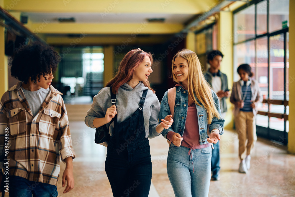 Happy teenage girls talk while walking through high school hallway.