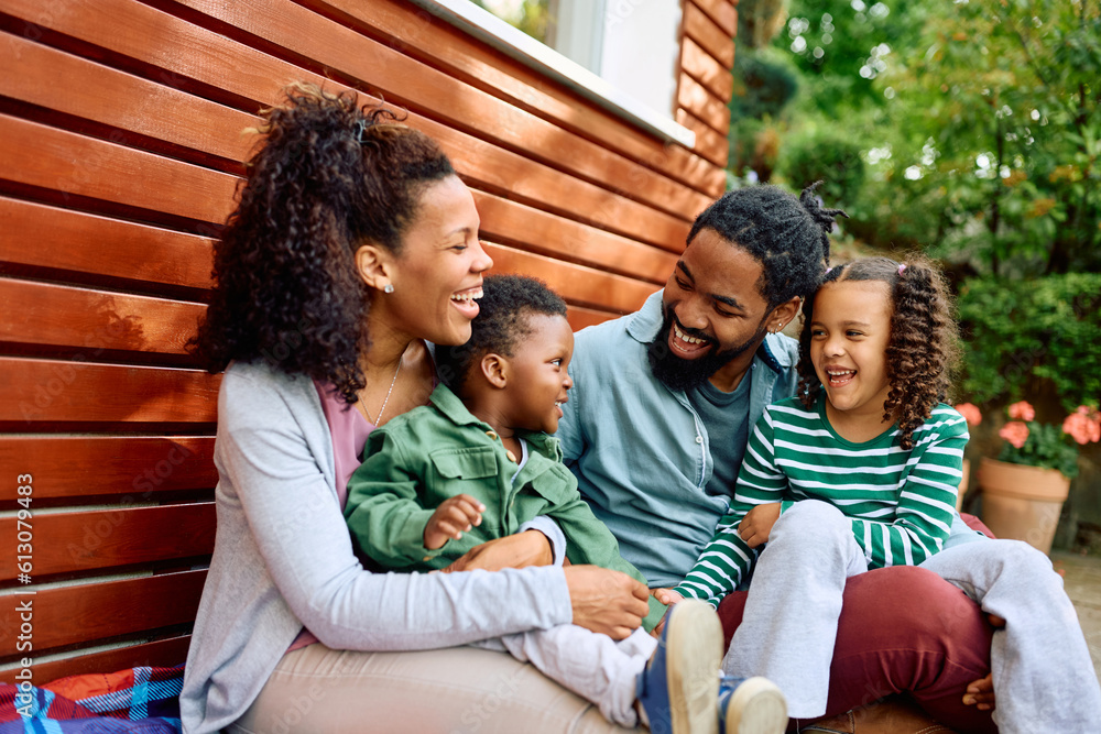 Happy black parents and their kids talk while relaxing in backyard.