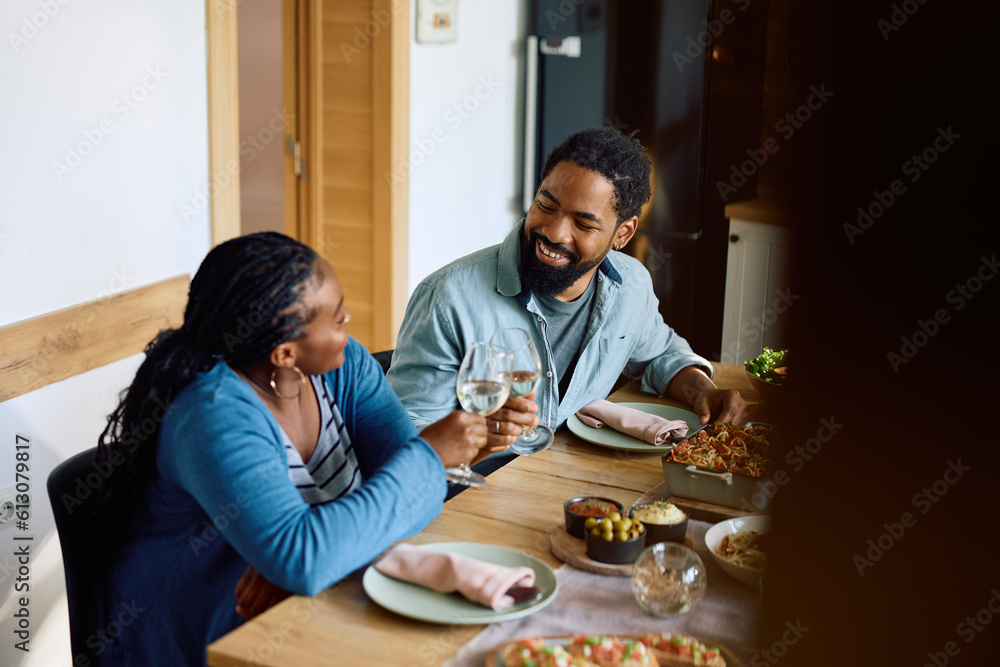 Fototapeta premium Happy black couple toasting with wine while eating at dining table.
