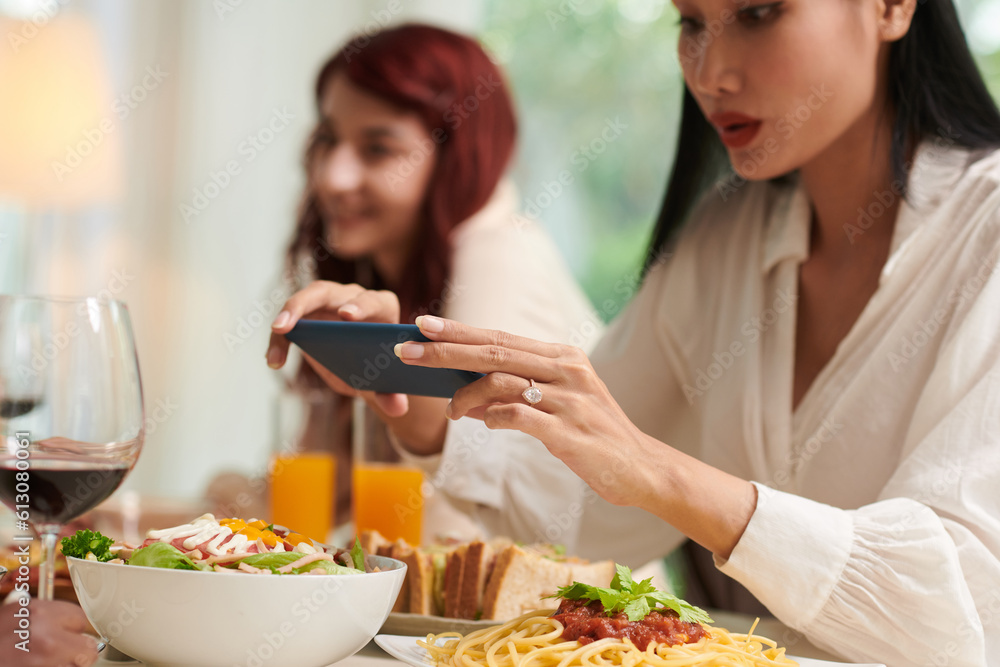 Hands of young Asian woman in white blouse taking photo of tasty homemade meals in bowl prepared for friends and guests Hands of young Asian woman in white blouse taking photo of tasty homemade meals in bowl prepared for friends and guests