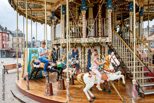 Slika na platnu Adorable little girl and school kid boy having a ride on the old vintage merry-go-round in city of Honfleur France