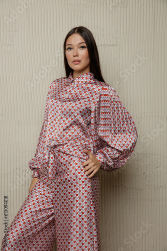 Wallpaper Mural High fashion photo of a beautiful elegant young asian woman in pretty rosy brown jumpsuit with pattern. Sandy beige textured wall Torontodigital.ca