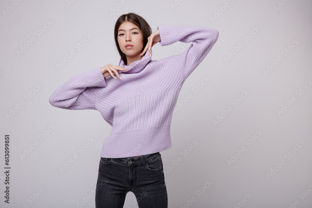 Fashion photo of a beautiful elegant young asian woman in a pretty pale purple, lilac, lavender sweater, blouse, black jeans, denim posing on white, soft gray background. Studio Shot. Slim figure Fashion photo of a beautiful elegant young asian woman in a pretty pale purple, lilac, lavender sweater, blouse, black jeans, denim posing on white, soft gray background. Studio Shot. Slim figure