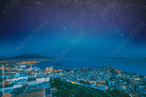 Naples, Italy. Skyline Cityscape In Evening Lighting. Tyrrhenian Sea And Landscape With Volcano Mount Vesuvius. City In Night Illuminations. Bold Bright Blue Azure Night Starry Sky With Glowing Stars.